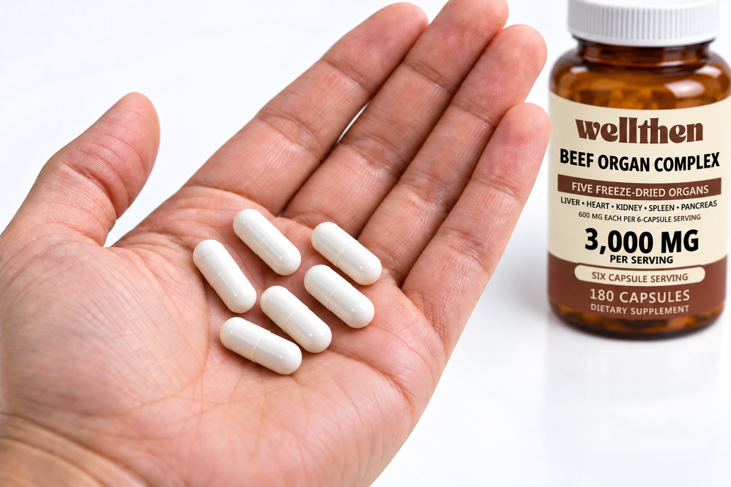 Six bovine organ capsules in a hand beside a finished beef organ complex bottle